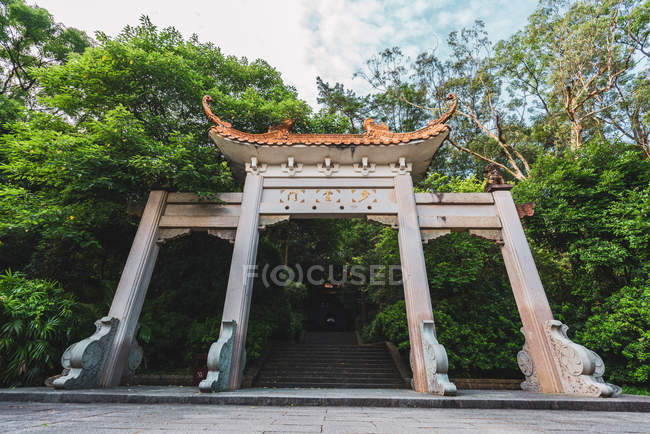 Ornamentales puertas de piedra oriental con escalera entre vegetación tropical, Qingxiu Montaña, China - foto de stock
