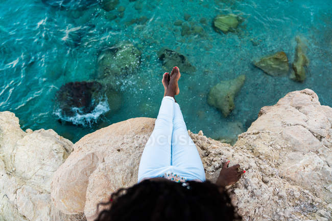 Woman sitting on cliff above crystal clear turquoise water — Stock Photo