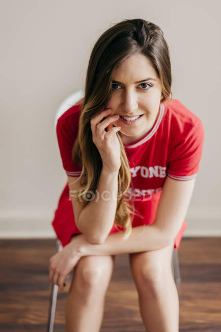 Smiling woman in red outfit sitting on chair and staring at camera — Stock Photo