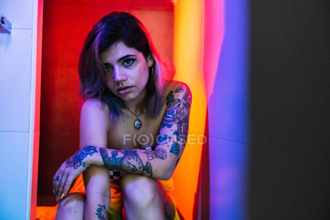Sensual jovem mulher com tatuagens olhando para a câmera enquanto posando no banheiro durante a festa — Fotografia de Stock