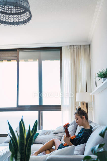 Зосереджена молода жінка грає на гітарі на дивані в сучасній стильній квартирі — стокове фото