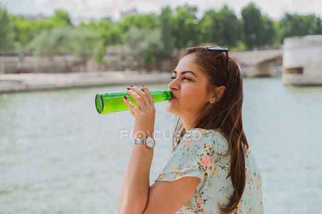 Молодая женщина в летнем платье пьет воду на набережной — стоковое фото