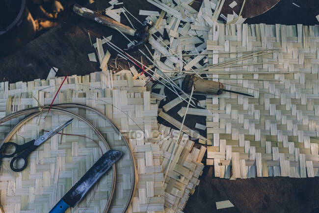 Вид зверху тканих листів із солом'яного листя з шилом, ножицями, ножем, молотком і рамкою для вишивання лежить на ньому — стокове фото