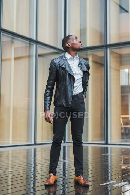 Hombre de negocios de pie en el pavimento contra el edificio de vidrio moderno - foto de stock