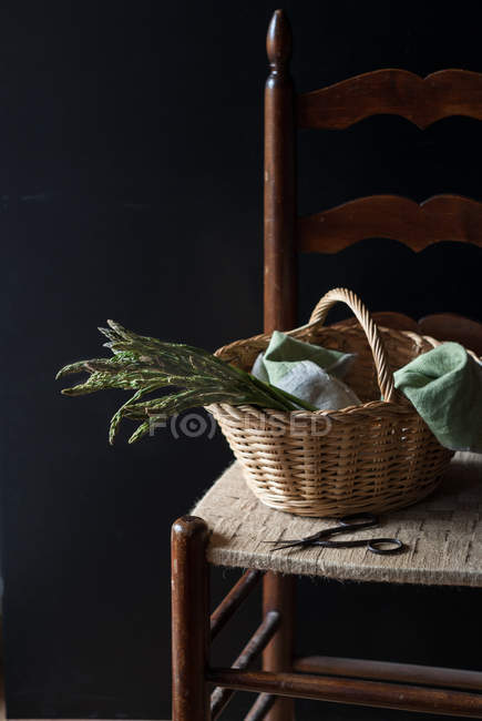 Cesta de espargos verdes frescos na cadeira no fundo preto — Fotografia de Stock
