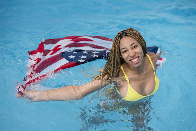Улыбающаяся женщина, стоящая в воде в бассейне с американским флагом — стоковое фото