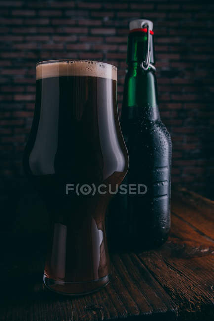 Stout beer in glass and bottle on dark wooden table — Stock Photo