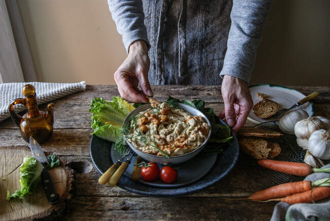 Hands taking plate with delicious artichoke hummus — Stock Photo