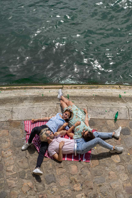 Amici sdraiati sulla coperta sul lungomare in estate — Foto stock