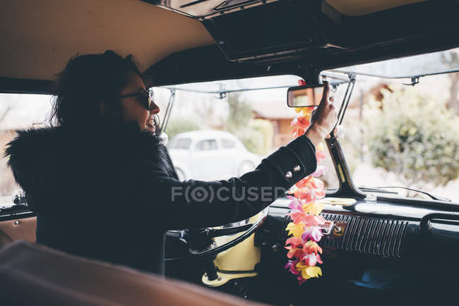 Jovem mulher verificando espelho retrovisor enquanto sentado no carro velho — Fotografia de Stock