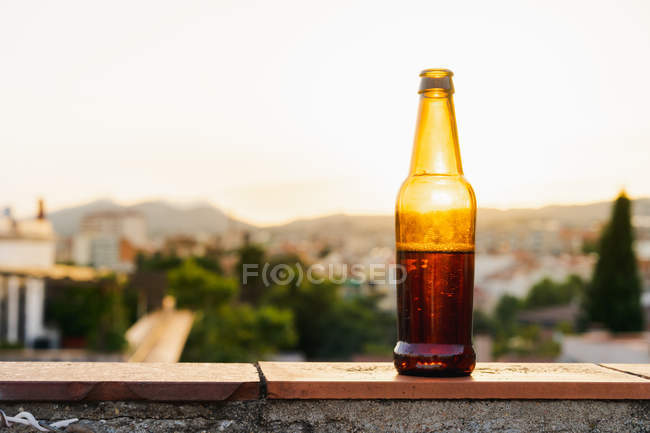 Відкрита коричнева скляна пляшка пива на парапеті даху на заході сонця — стокове фото
