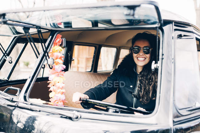 Retrato de jovem mulher de casaco preto e óculos de sol sentado dentro do carro — Fotografia de Stock