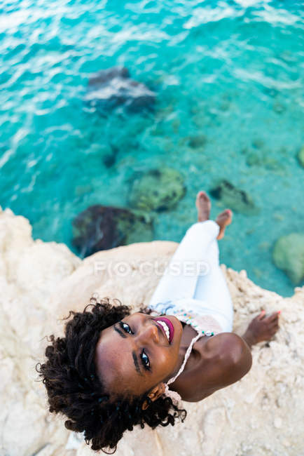 Жінка, сидячи на скелі над бірюзові води і, дивлячись на камеру — стокове фото