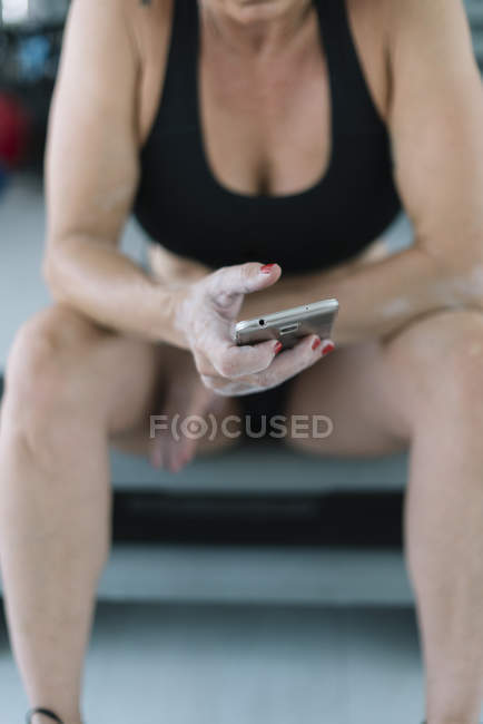 Atleta do sexo feminino sentado no banco e usando aplicativo de fitness no smartphone — Fotografia de Stock