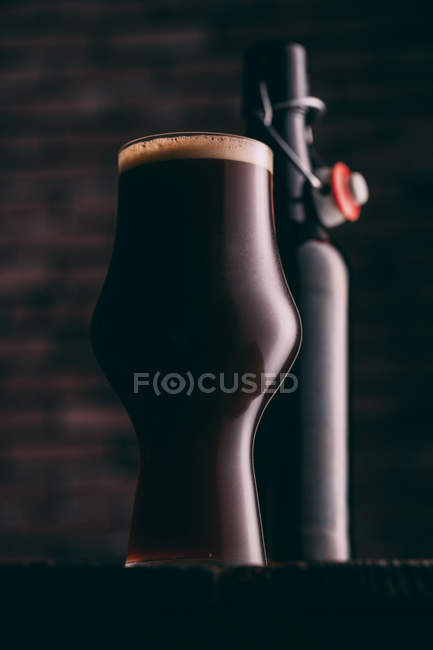 Stout beer in glass and bottle on dark wooden table — Stock Photo