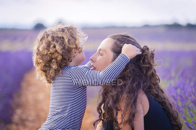 Mulher e pequena filha encaracolada se divertindo no campo de lavanda violeta florescendo — Fotografia de Stock