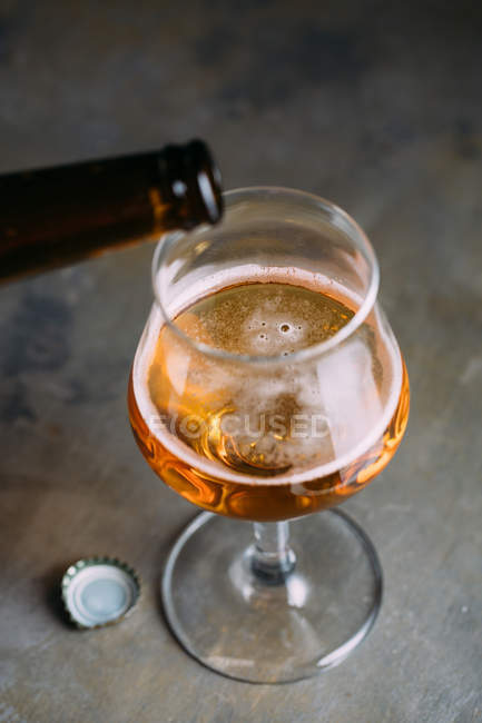 Derramando cerveja em vidro de garrafa no fundo cinza — Fotografia de Stock
