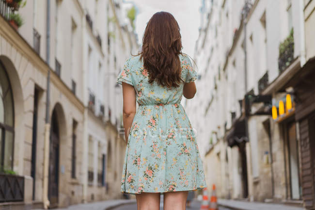 Вид сзади молодой женщины в узорчатом цветочном платье, стоящей на улице — стоковое фото