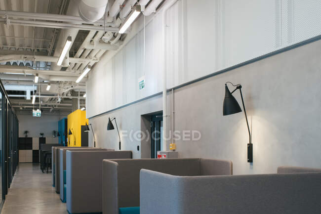 Interior gris de la cafetería de oficina con mesas vacías y sofás con respaldos altos y lámparas colgando en las paredes - foto de stock