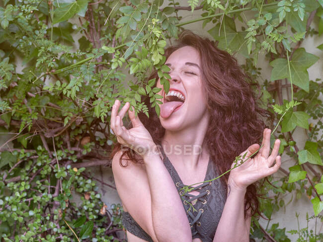 Charmante jeune femme en soutien-gorge essayant de lécher les feuilles d'arbre tout en se tenant dans le jardin — Photo de stock