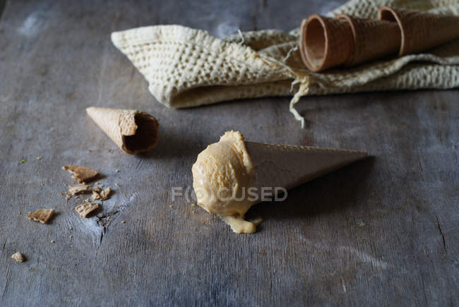 Вкусное мороженое в хрустящем сахарном конусе с пустыми конусами на сером деревянном столе — стоковое фото