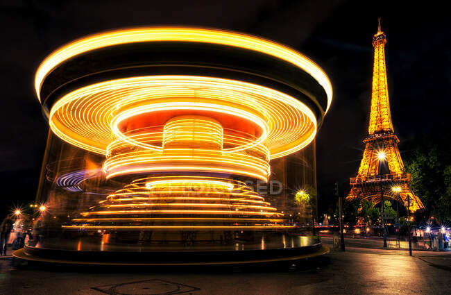 Bright traces of light on spinning carousel near magnificent Eiffel Tower at night in Paris, France. — Stock Photo
