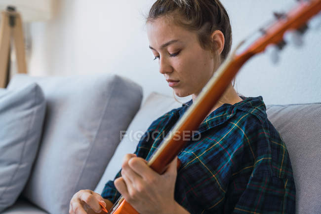 Jeune femme jouant de la guitare sur canapé — Photo de stock
