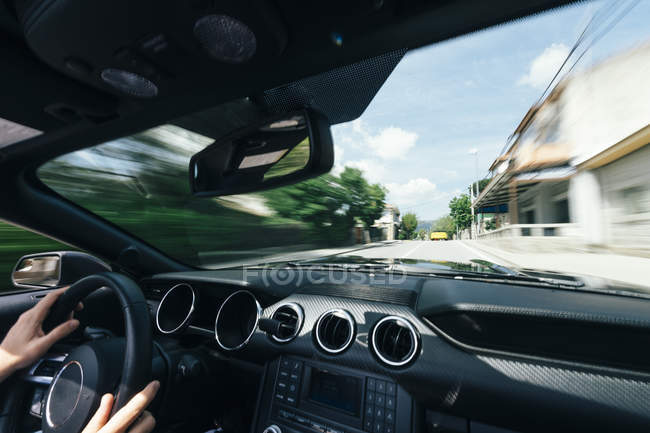 Male hands on steering wheel of driving car down street with blurred view behind glass — Stock Photo