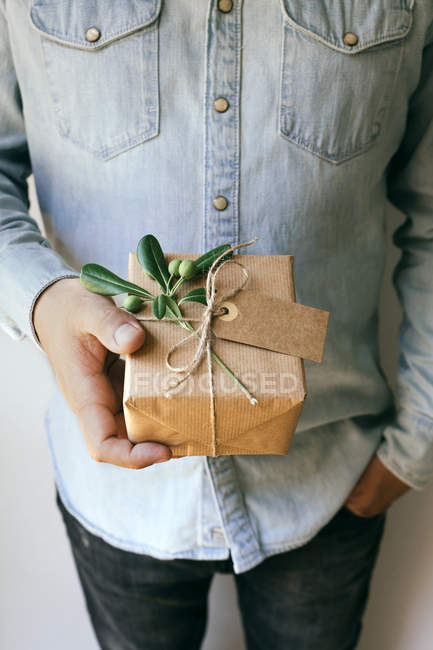Мужчина держит самодельный завернутый подарок украшенный зеленой веткой — стоковое фото