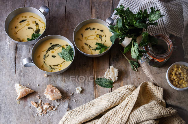Corn cream soup with coconut and pesto in bowls on wooden table with ingredients — Stock Photo