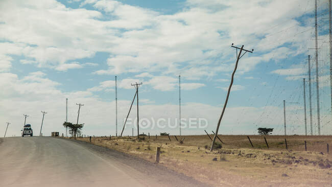 Auto fährt in Wüste mit umstürzenden Strommasten auf Straße — Stockfoto
