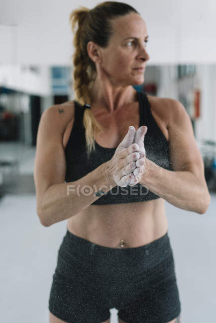 Femme écartant la craie sur les mains tout en s'entraînant dans la salle de gym — Photo de stock