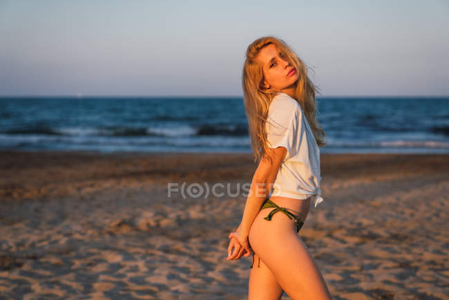 Relaxed blond woman in bikini and shirt standing on beach — Stock Photo