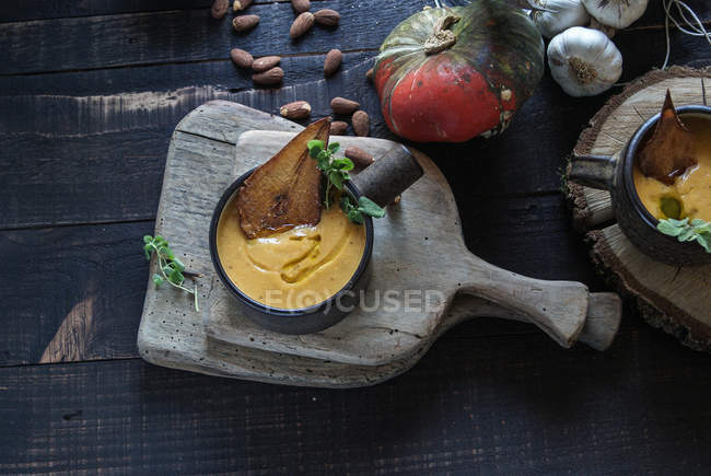 Sopa de crema de calabaza servida con peras secas sobre una mesa rústica de madera con ingredientes - foto de stock