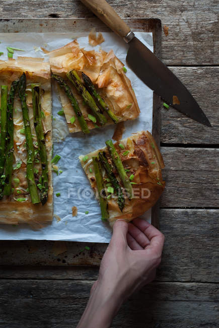 Human hand taking piece of asparagus pie — Stock Photo