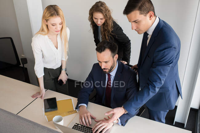 Colaboradores elegantes que se reúnen alrededor del ordenador portátil en la oficina - foto de stock
