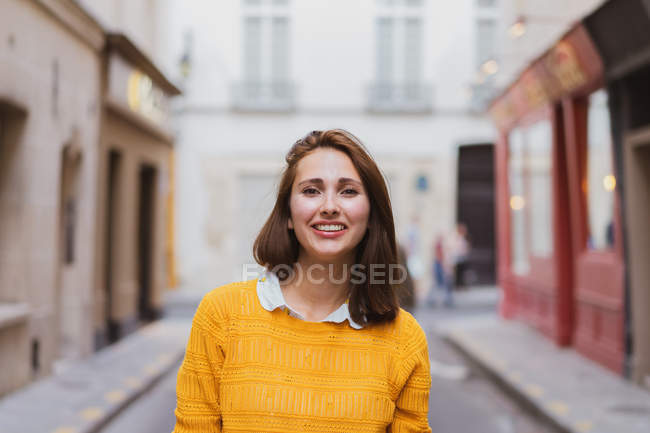 Улыбающаяся женщина в желтом кардигане стоит на улице и смотрит в камеру — стоковое фото