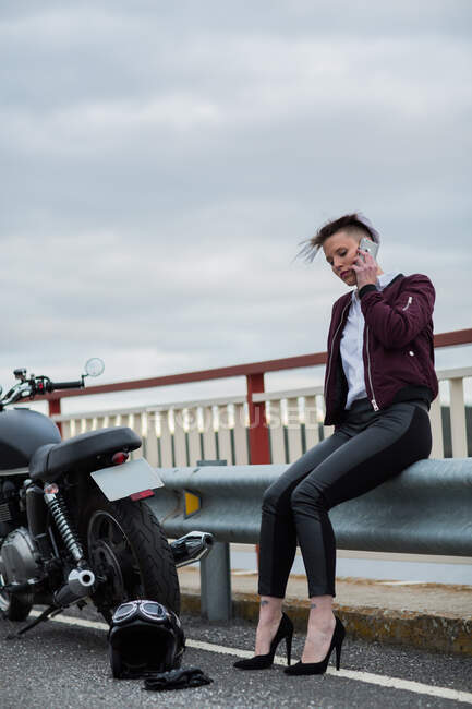 Приваблива жінка розмовляє зі смартфоном поруч з її ретро мотоциклом — стокове фото