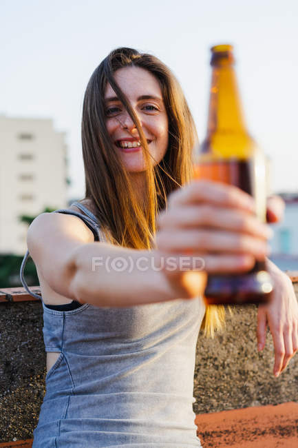 Щаслива жінка показує пляшку коричневого пива на даху — стокове фото
