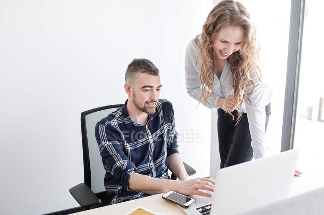 Улыбающаяся женщина и мужчина за рабочим столом смотрят ноутбук вместе и работают в команде в современном офисе — стоковое фото