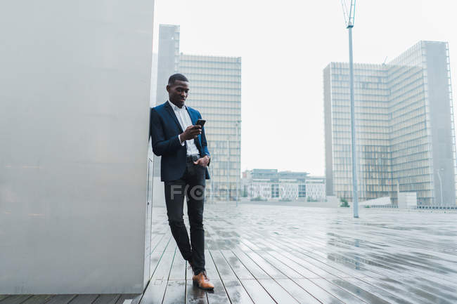 Uomo d'affari afroamericano che utilizza lo smartphone mentre si trova nella città moderna — Foto stock
