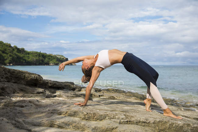 Fit woman in sportswear doing yoga and stretching back on beach in Bali, Indonesia — Stock Photo