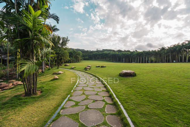 Stone-paved walkway on green terrain of lush tropical park of Qingxiu Mountain with trees, China — Stock Photo