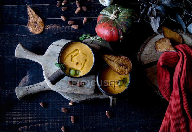 Soupe à la crème de citrouille servie avec des poires séchées dans des bols sur une table en bois rustique avec des ingrédients — Photo de stock