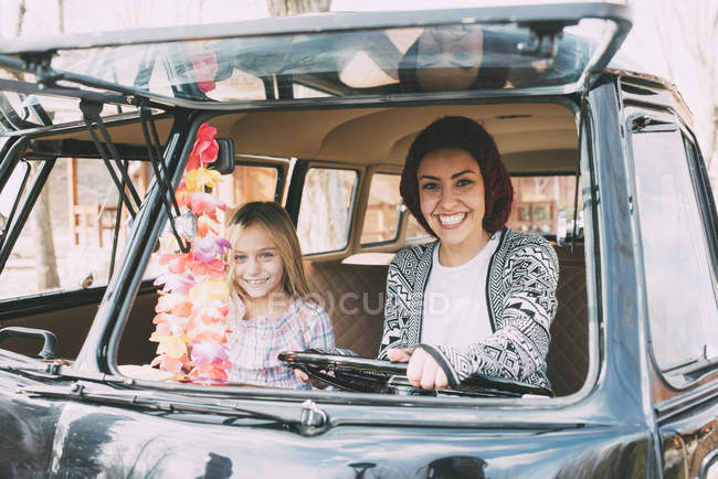 Mujer joven y chica rubia sentada en coche viejo - foto de stock
