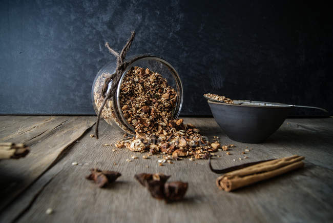 Frasco virado de granola deliciosa com especiarias chai na mesa de madeira com tigela e vários aromas — Fotografia de Stock