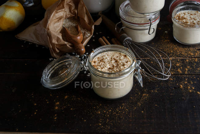 Frascos de vidro de sobremesa doce de arroz com leite e canela em mesa de madeira com ingredientes — Fotografia de Stock
