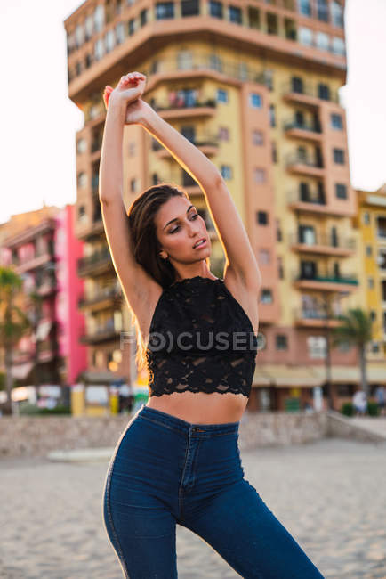 Sinnliche brünette Frau posiert am Strand mit Gebäuden im Hintergrund — Stockfoto