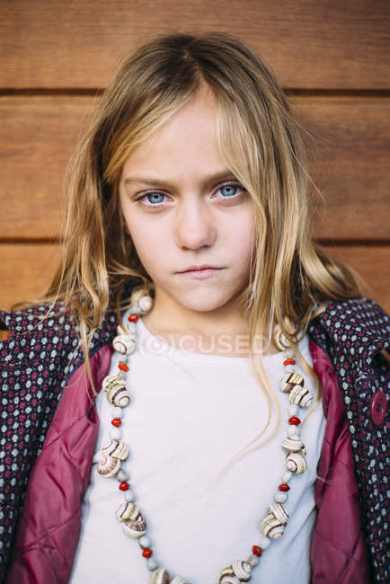 Retrato de menina loira com olhos azuis de pé fundo de madeira — Fotografia de Stock