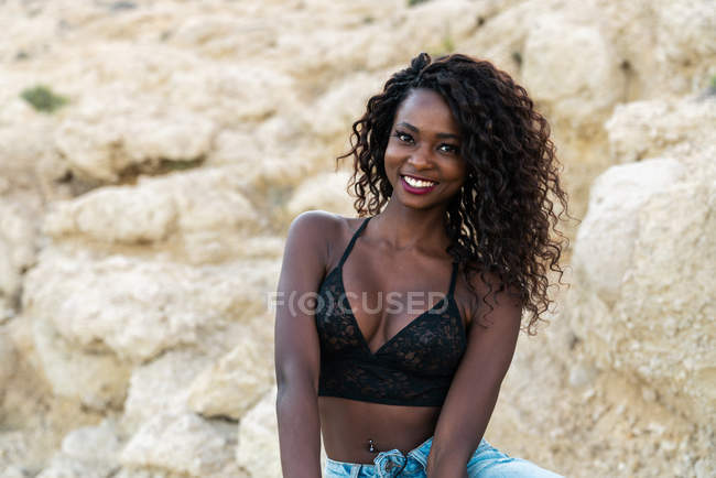 Charmante femme noire en dentelle haut regardant caméra contre falaise — Photo de stock